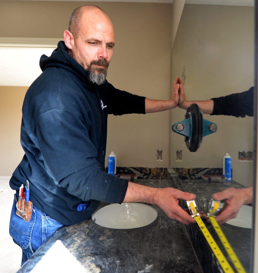 Rainbow Glass employee carefully measures using a measuring tape during new mirror installation